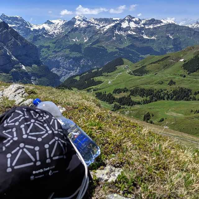 A backpack with the GraphQL logo sits atop a swiss mountain